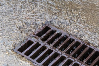 Fragment of the cast iron grid of the storm drain mounted in a concrete surface and flowing down rainwater with small debris during a rain