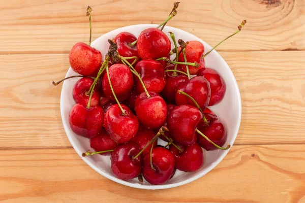 Washed red sweet cherries on stems covered with water drops in the white bowl on the rustic table, top view