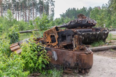 Russian tank destroyed during hostilities in Russian invasion of Ukraine, 2022 and torn down gun turret of another tank on a foreground on a forest edge next a road.