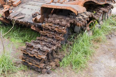 Remains of the Russian tank destroyed during hostilities in Russian invasion of Ukraine, 2022. Rusty broken tracks with molten track rollers among the grass on a forest edge.