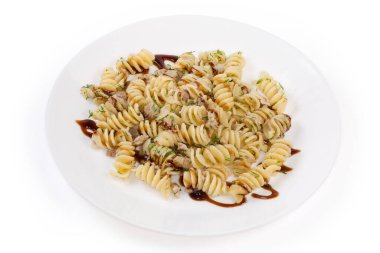 Prepared spiral pasta, also known as fusilli or rotini pasta mixed with stuffing of boiled chopped pork, fried onion, fresh greens and sauce on a white dish on a white background