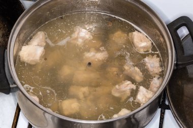 Meat broth in a stainless steel pot during the cooking on a stove top