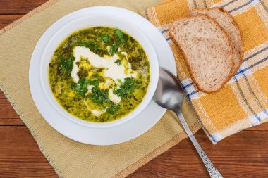 Serving of the sorrel soup, also known as green borscht with chopped hard-boiled egg and sour cream in a white bowl, slices of bread on a napkin on an old rustic table, top view
