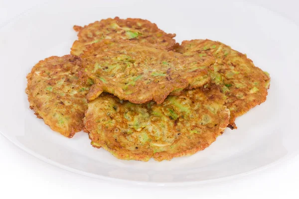 Fried small thick savory zucchini pancakes on the white dish on a white background close-up in selective focus