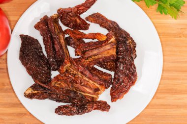 Sun-dried red tomatoes on a white dish on a wooden surface, top view