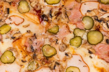 Surface of the pizza with different ham, mushrooms and pickled cucumbers, top view of pizza fragment, background