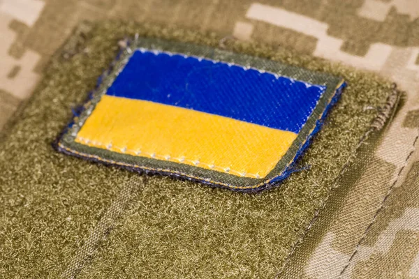 Textile Ukrainian flag sticker with hook-and-loop fastener fixed on a military camouflage uniform, close-up in selective focus