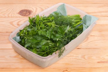 Stems of the freshly harvested dill and parsley in white plastic container with paper napkin on the rustic table