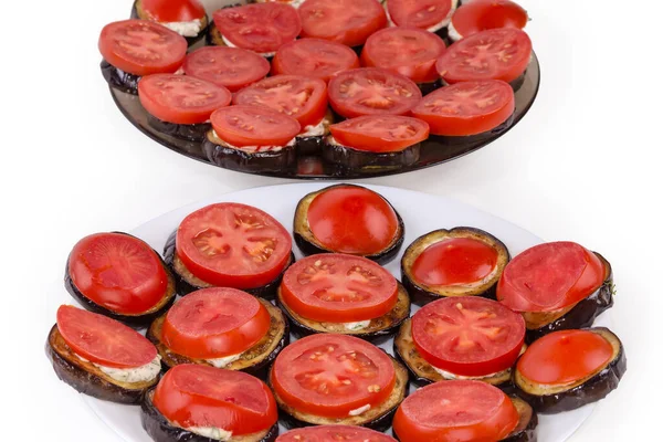 用大蒜酱汁切碎的圆形茄子烤着 然后在两个不同的菜盘上切下几圈新鲜的西红柿 放在一个白色的背景上 有选择性地将其切碎 — 图库照片