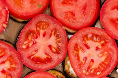 Daireler halinde, sarımsak soslu patlıcanlar tarafından kızartılmış ve koyu tabakta kesilmiş taze domates çemberleri ile kaplanmış.