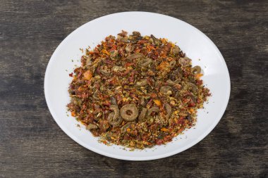 Makarna için farklı baharat ve kurutulmuş sebzelerin karışımı ve siyah bir yüzey üzerindeki beyaz tabağın üzerindeki diğer yemekler.