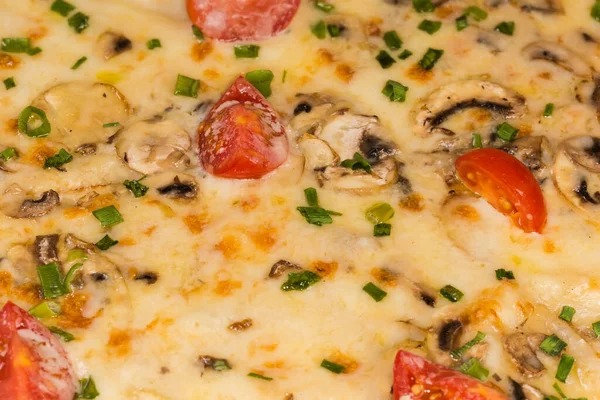 Cooked spicy pizza with meat, mushrooms, cherry tomatoes, fragment close-up in selective focus