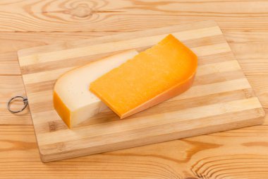 Kırsal bir masada tahta bir bambu kesme tahtasının üzerinde iki parça yarı sert peynir.