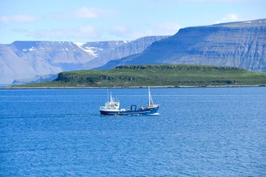 Large boat with blue fishermen's hull in the northern sea of Europe and mountains with snow as a backdrop - Iceland