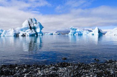 So many pieces of ice with black parts due to the volcanic ash floating on the calm water of the Jokulsarlon lake and part of the beach with black stones
