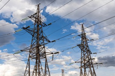 Paslı elektrik hattı mavi gökyüzünde beyaz bulutların ardında.