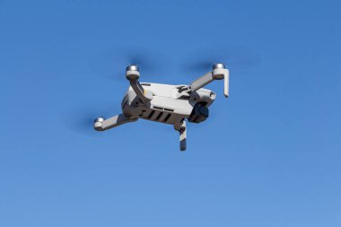 The Gray unmanned aerial vehicle with four propellers and blades is flying on the blue sky background