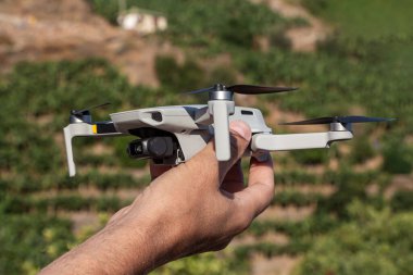 A Man is launching a gray drone with a with four propellers and blades in his hands in sunny summer day