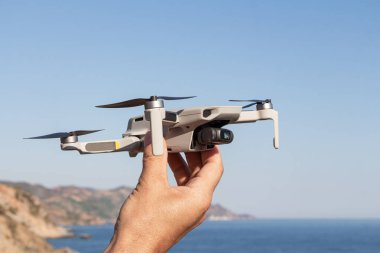 A Man is launching a gray drone with a with four propellers and blades in his hands in sunny summer day