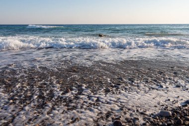 Renkli yumuşak taşların güzel bir dokusu dalgalar ve köpüklerle mavi denizin kıyısında.