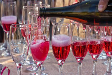 A Man pouring red wine into glasses from a brown bottle in the sunny day on the holiday