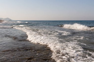 Renkli yumuşak taşların güzel bir dokusu dalgalar ve köpüklerle mavi denizin kıyısında.