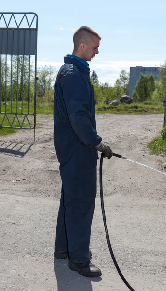 Werknemer in Amerikaanse overalls drenken gebied met water uit een slang — Stockfoto