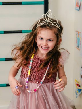a little girl in a beautiful dress and crown plays and runs around the house.
