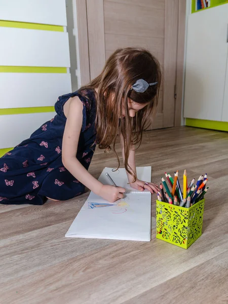 Niña dibuja con lápices en el suelo en su habitación. Imágenes de stock libres de derechos