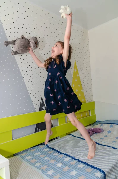 한 어린 소녀가 침대에서 뛰고 놀면서 웃고 있습니다. 로열티 프리 스톡 이미지