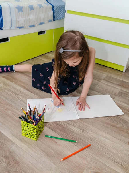 Klein meisje tekent met potloden op de vloer in haar kamer. Stockfoto