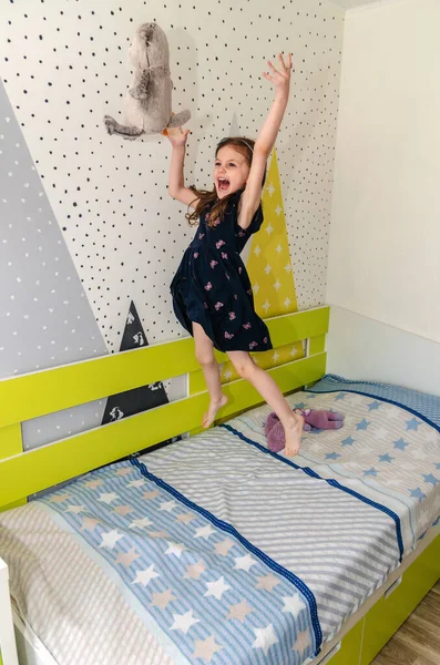 Una niña está saltando y jugando en su habitación en la cama y riendo. Imagen de archivo