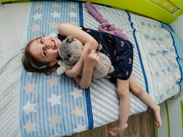 一个小女孩把她柔软的玩具抱在房间的床上. 免版税图库照片