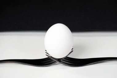Close-up of a white egg balancing on a pair of black forks on white 