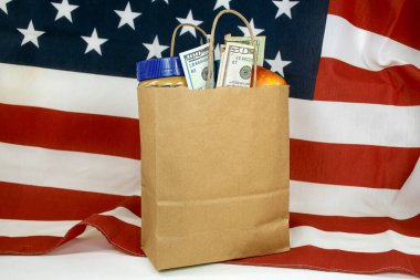Bir Amerikan bayrağının üzerinde içi yiyecek ve para dolu düz kahverengi bir kese kağıdı.  