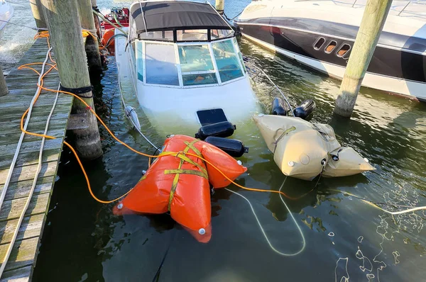 White sinking power boat being salvaged by marine airbags in a marina slip