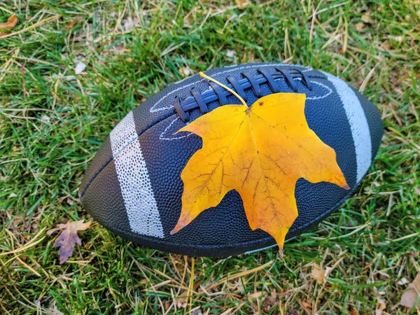 Zwart Voetbal Met Een Gele Herfst Esdoorn Blad Gras — Stockfoto