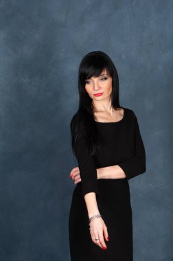 Etkileyici ve büyüleyici güzel bir kız, siyah elbiseli esmer. Güzel ve ince bir kadın üzgün ve düşünceli, tek renkli mavi, modaya uygun, pejmürde bir arka planda stüdyo portresi