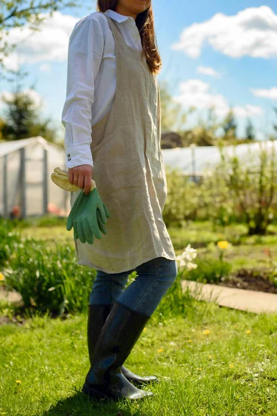 在一个阳光灿烂的日子里 一位穿着亚麻布围裙 戴着园艺手套 站在院子里准备种花的年轻女子 — 图库照片