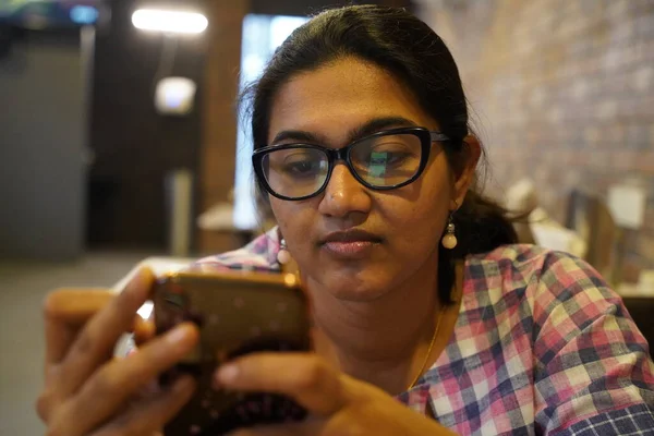 Μια νεαρή κοπέλα με γυαλιά κοιτάζει προσεκτικά το τηλέφωνό της με επιλεκτική εστίαση στο πρόσωπο — Φωτογραφία Αρχείου
