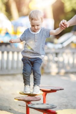 Parktaki küçük çocuk engelli parkurunu geçiyor. Vücut koordinasyonu ve denge egzersizleri bir annenin yardımıyla..