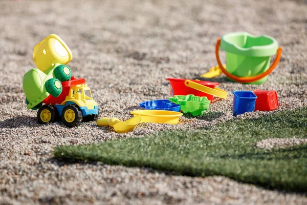 Colorful plastic toys for playing in an outdoor sandbox. Toy sand pails and shovels over a gravel background.