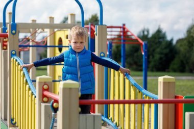 Sevimli, sarışın bir çocuk modern renkli açık hava çocuk parkında yürüyor..