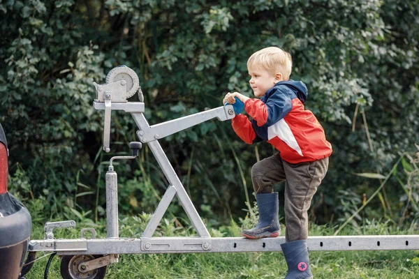 An agile child sports on a boat trailer mechanism in nature.