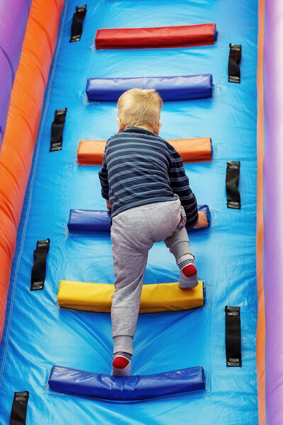 Brave little boy child climbs the stairs of a multi-colored slide in the attraction park.