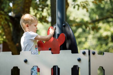 Küçük çocuk, çocuk parkında kendinden emin bir şekilde oyuncak bir geminin dümenini çeviriyor..