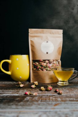 Tahta masada ekolojik ambalajda kuru çay. Bir fincan bitki çayı ve sarı kupa.