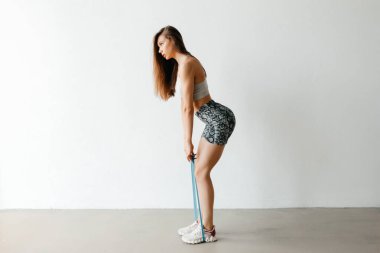 Alt vücut kasları için direnç bandıyla egzersiz yapan spor kıyafetleri ve spor ayakkabıları giyen atletik bir kadın.