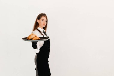 Siyah önlüklü zarif bir garsonun portresi bir pastanede müşteriye hizmet ediyor, kruvasan veriyor.