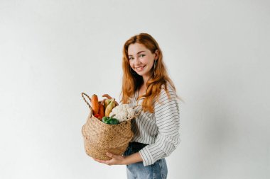 Beyaz arka planda izole edilmiş alışveriş sepeti olan genç, gülümseyen bir aşçı. Beyaz arka planda sebze ve meyve sepeti olan bir kız..